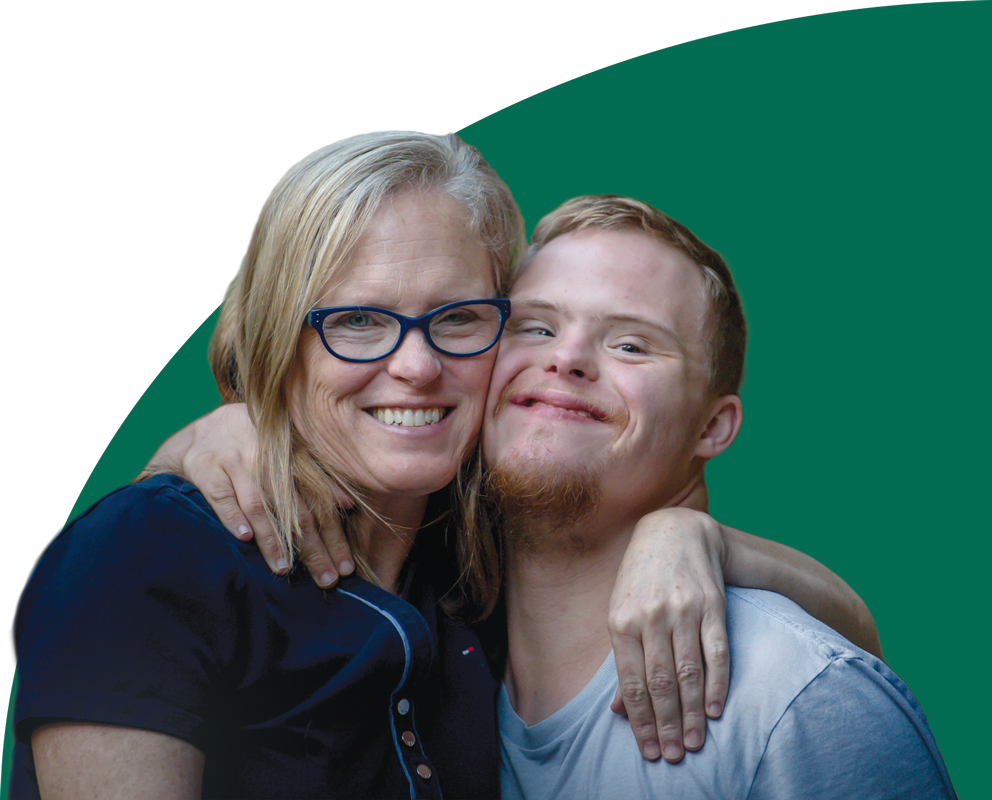 A young man with a disability smiles with his arm around a family member