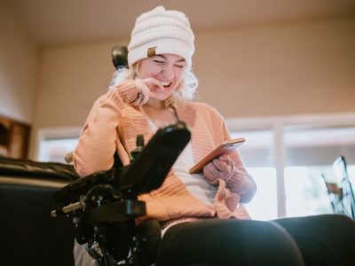 A young woman with cerebral palsy smiles while browsing social media apps on her phone